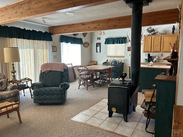 living area featuring a textured ceiling, light tile patterned flooring, light colored carpet, beamed ceiling, and a wood stove