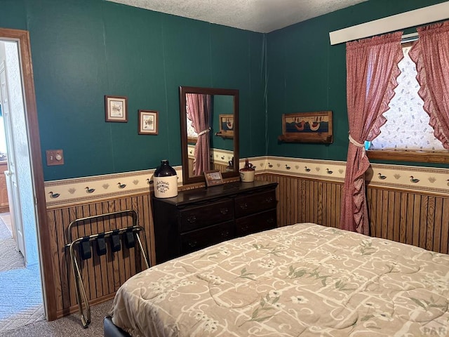 bedroom featuring a wainscoted wall, carpet floors, and a textured ceiling