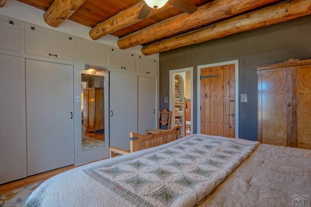 bedroom with multiple closets, light wood-type flooring, wooden ceiling, and beamed ceiling