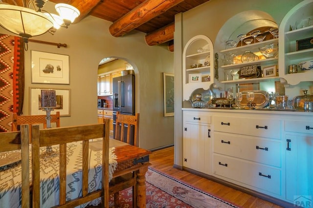 interior space featuring built in features, arched walkways, an inviting chandelier, light wood-style floors, and beam ceiling