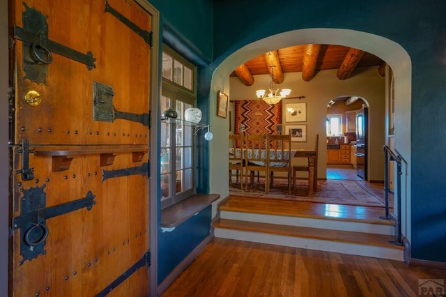 interior space featuring arched walkways, beam ceiling, a notable chandelier, and wood finished floors