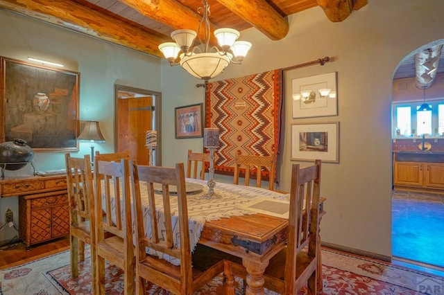 dining area featuring arched walkways, a notable chandelier, and beamed ceiling