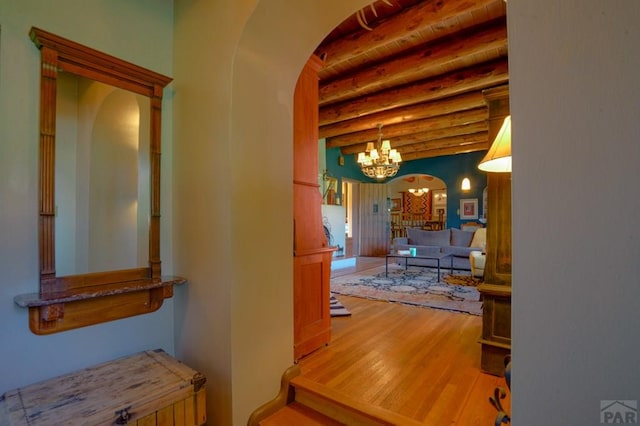 hallway with arched walkways, wood ceiling, light wood-style flooring, beamed ceiling, and a chandelier