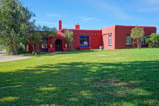 pueblo-style home featuring a chimney and a front lawn