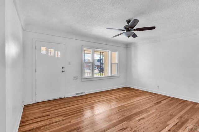 entrance foyer featuring a textured ceiling, a ceiling fan, baseboards, visible vents, and light wood-style floors