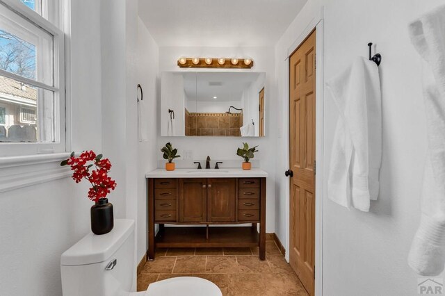 bathroom featuring baseboards, tiled shower, vanity, and toilet