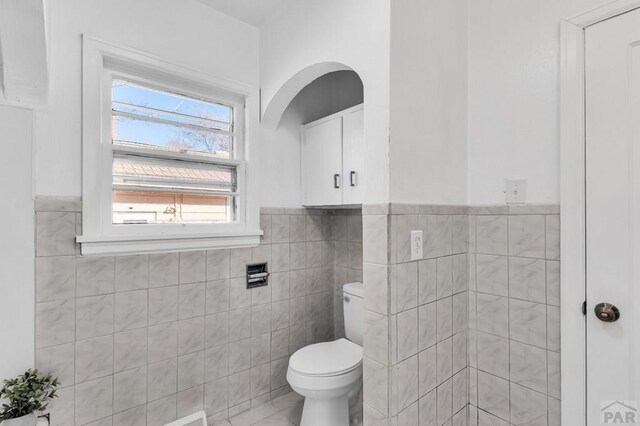 half bathroom featuring toilet, tile walls, and wainscoting