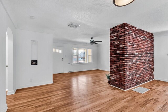 unfurnished living room featuring arched walkways, visible vents, light wood-style flooring, ceiling fan, and a textured ceiling