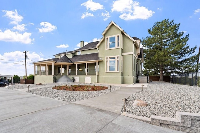 view of front of house with a chimney, stucco siding, a porch, a shingled roof, and fence