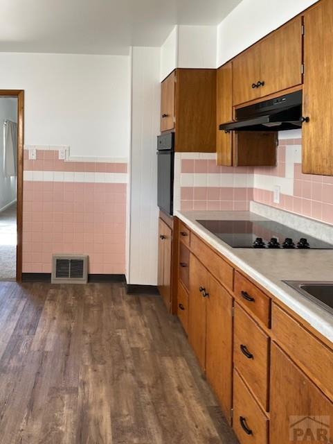 1640 Wabash Ave, Pueblo, CO 81004 - kitchen with black appliances, under cabinet range hood, brown cabinets, dark wood finished floors, and wainscoting