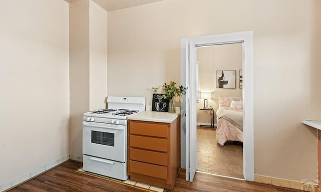 kitchen featuring dark wood-type flooring, light countertops, baseboards, and white gas range oven