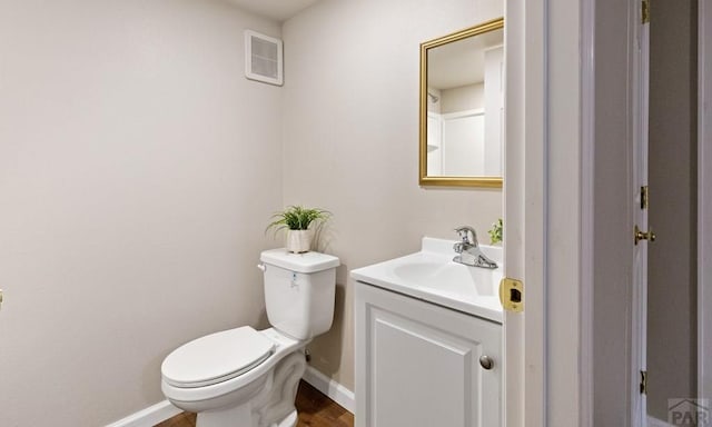 half bath with toilet, visible vents, vanity, and baseboards