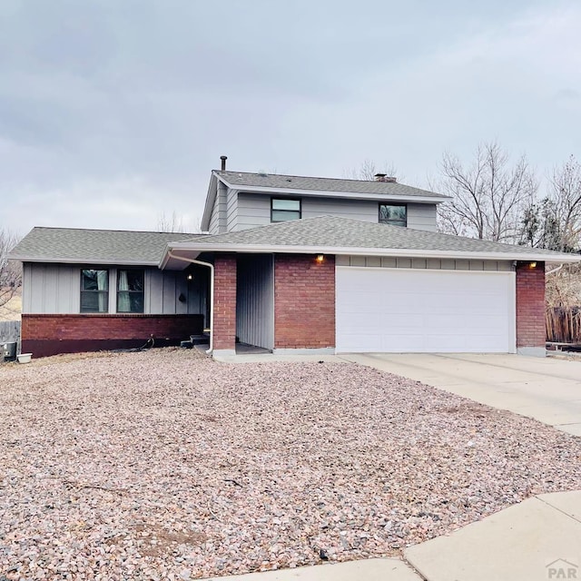 view of front facade with an attached garage, a shingled roof, concrete driveway, and brick siding