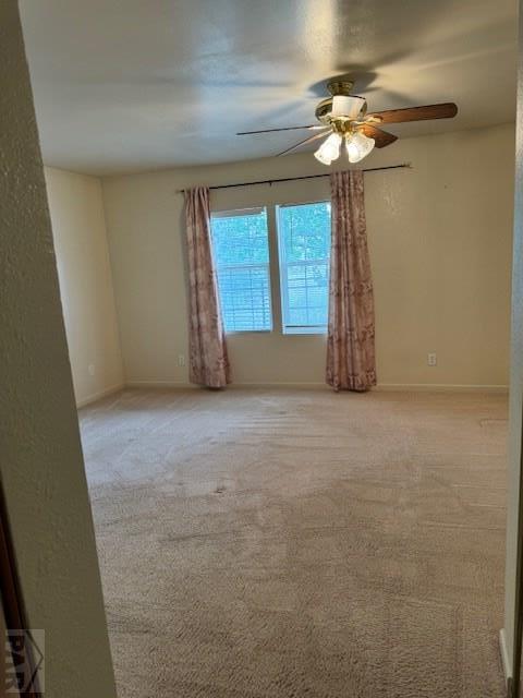 spare room with light carpet, ceiling fan, and baseboards