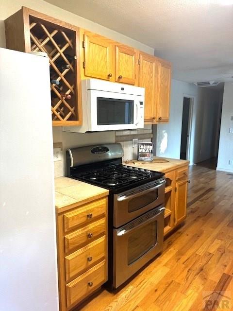 kitchen with white appliances, tasteful backsplash, light wood finished floors, visible vents, and tile counters