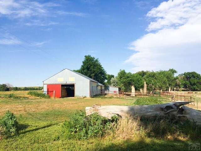 view of yard featuring a detached garage, a rural view, a pole building, fence, and an outdoor structure