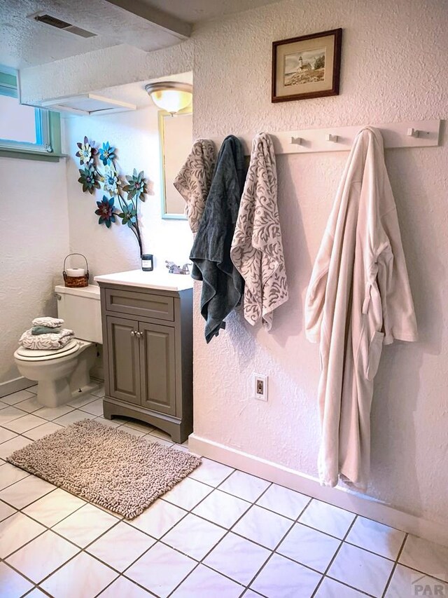 bathroom featuring visible vents, a textured wall, toilet, vanity, and tile patterned floors