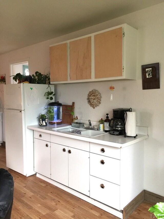 kitchen featuring a sink, white cabinetry, light countertops, freestanding refrigerator, and light wood finished floors