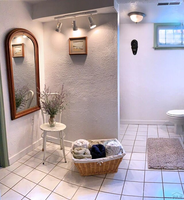 bathroom with toilet, a textured wall, baseboards, and tile patterned floors