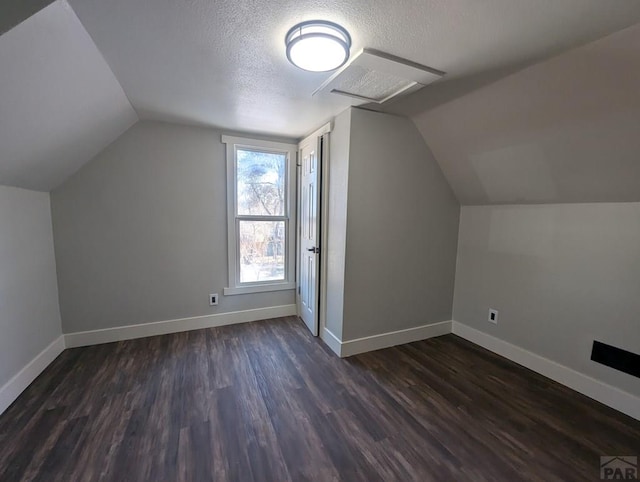 additional living space featuring a textured ceiling, dark wood-style flooring, lofted ceiling, and baseboards