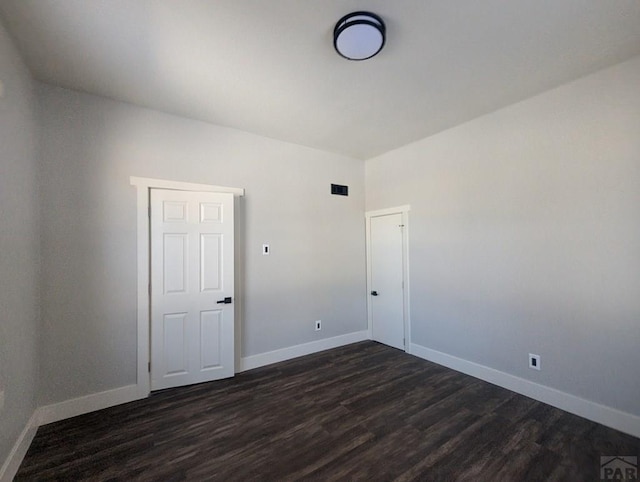 spare room with dark wood finished floors, visible vents, and baseboards