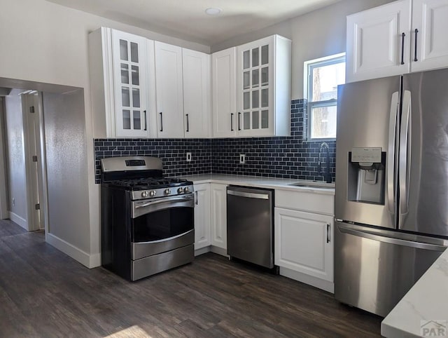 kitchen with stainless steel appliances, a sink, white cabinetry, dark wood finished floors, and glass insert cabinets