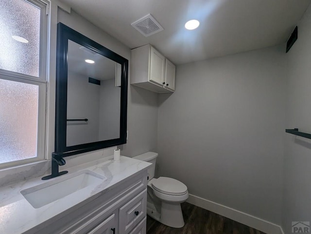 half bathroom with visible vents, toilet, vanity, wood finished floors, and baseboards