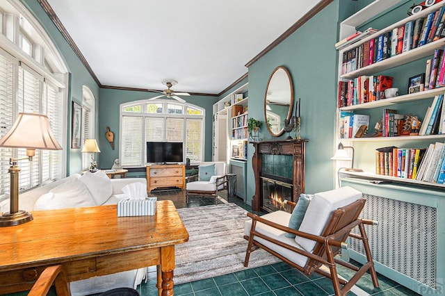 living area with a wealth of natural light, a glass covered fireplace, crown molding, and dark tile patterned floors