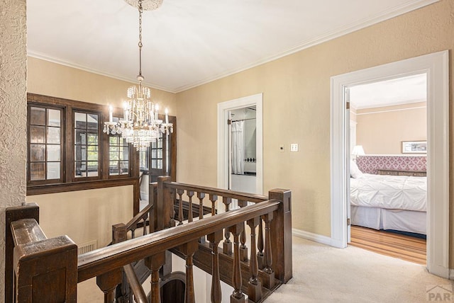 hallway with light carpet, crown molding, an upstairs landing, baseboards, and an inviting chandelier