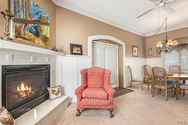 living area featuring a warm lit fireplace, arched walkways, wainscoting, light colored carpet, and ornamental molding