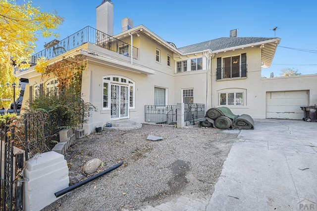 back of house featuring an attached garage, a balcony, driveway, stucco siding, and a chimney