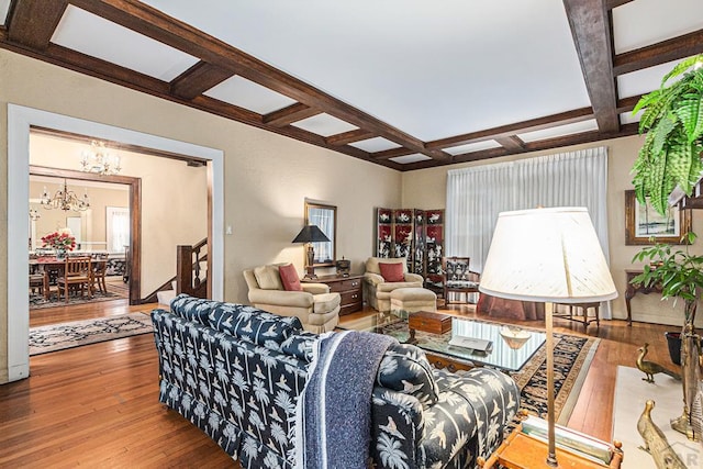 living room with coffered ceiling, an inviting chandelier, and wood finished floors