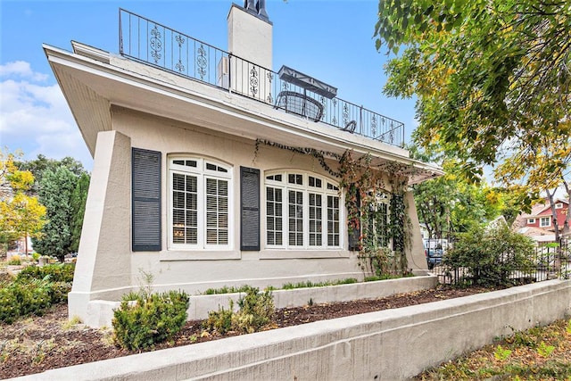 view of side of property with fence, a balcony, and stucco siding