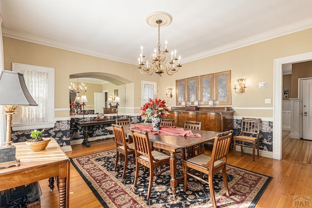 dining space with ornamental molding, arched walkways, light wood finished floors, and an inviting chandelier