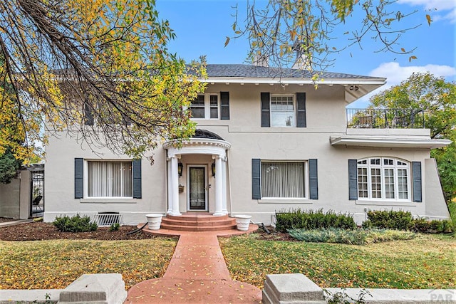 view of front of house with a balcony, a front yard, and stucco siding