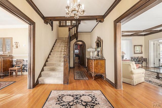 foyer featuring arched walkways, beam ceiling, stairway, and wood finished floors