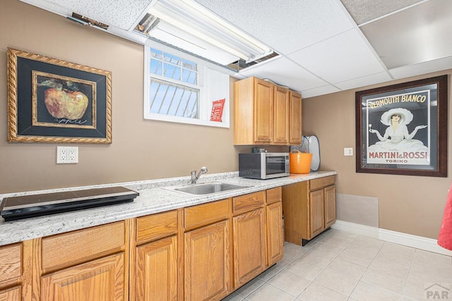 kitchen with stainless steel microwave, light tile patterned flooring, a sink, a drop ceiling, and baseboards