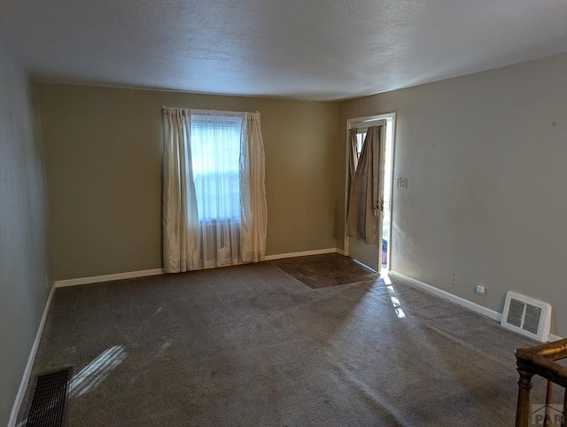 spare room featuring baseboards, visible vents, dark carpet, and a textured ceiling