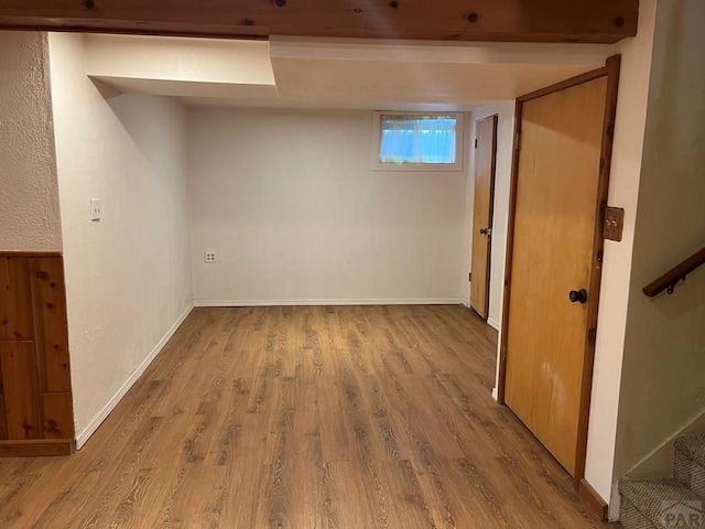 basement featuring light wood-style flooring, stairway, and baseboards