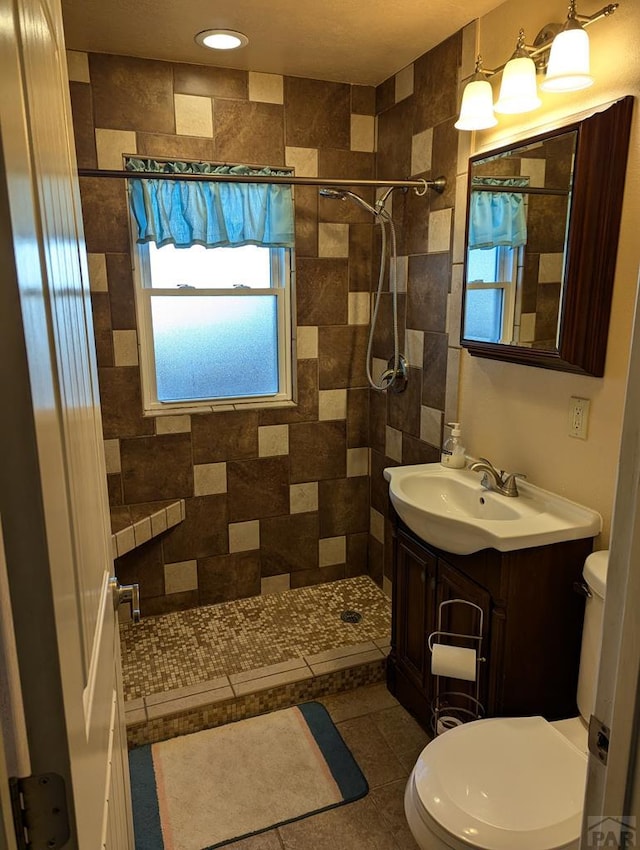 bathroom featuring vanity, a tile shower, toilet, and tile patterned floors