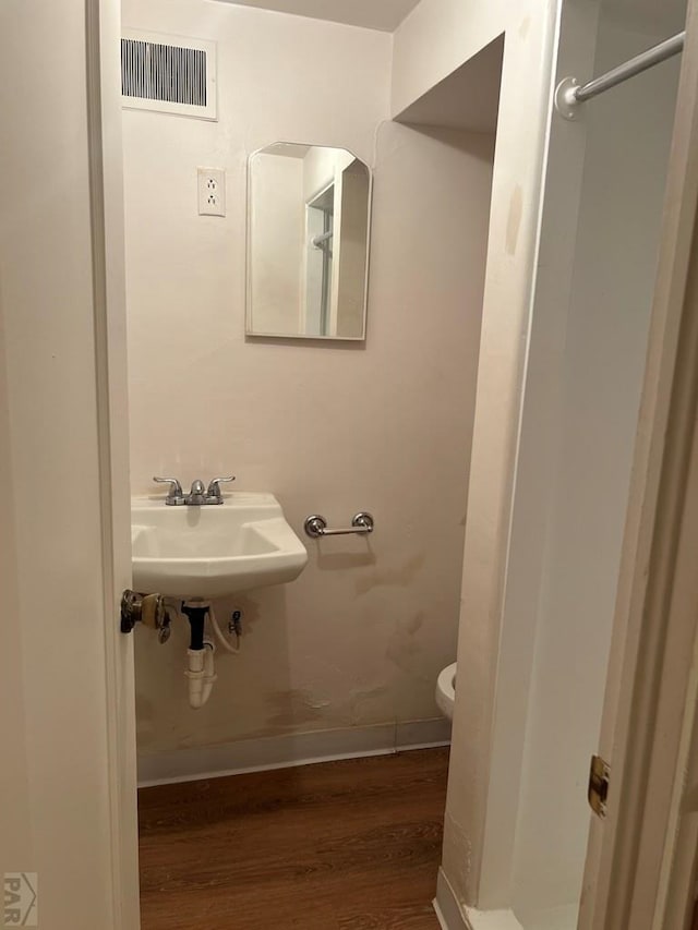 bathroom featuring toilet, a sink, wood finished floors, visible vents, and baseboards