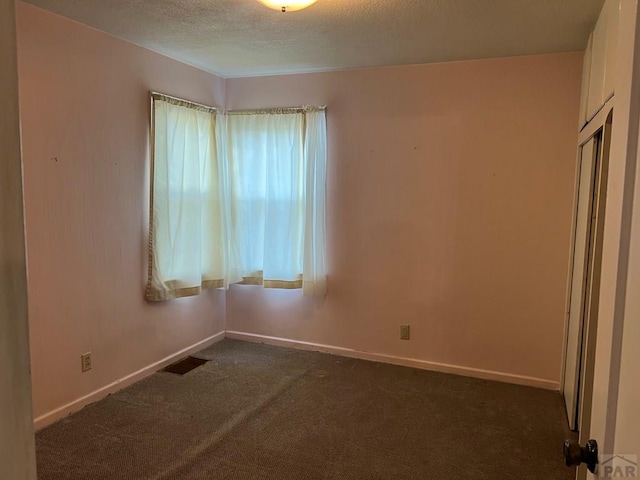 empty room with visible vents, baseboards, dark colored carpet, and a textured ceiling