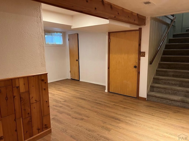 basement featuring light wood finished floors, visible vents, a textured wall, stairway, and baseboards