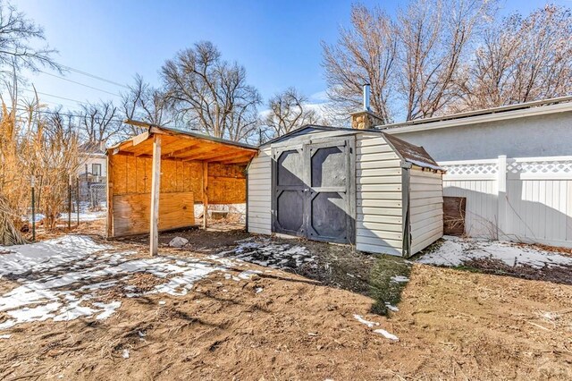 snow covered structure featuring fence, a storage unit, and an outdoor structure