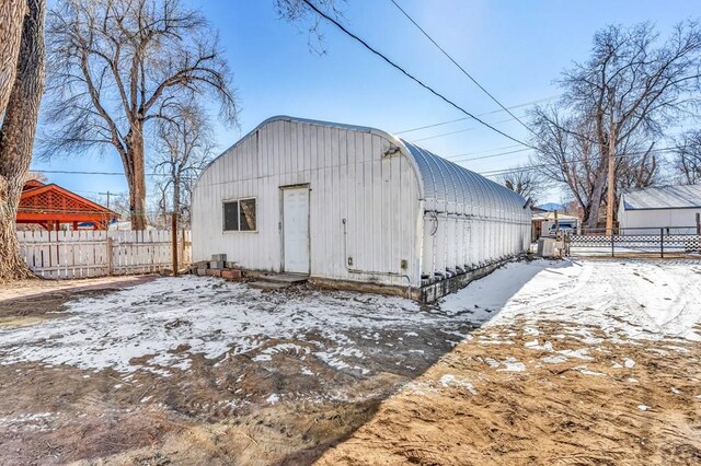 snow covered structure with fence and an outdoor structure