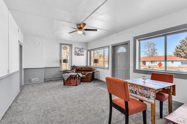 living area with ceiling fan, a baseboard heating unit, carpet floors, visible vents, and wainscoting