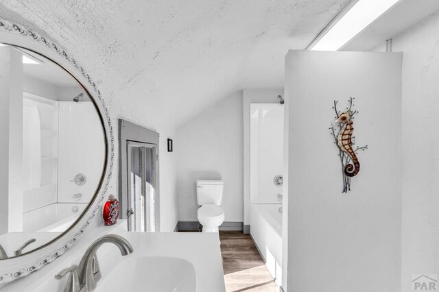 full bath featuring lofted ceiling, toilet, a sink, wood finished floors, and washtub / shower combination