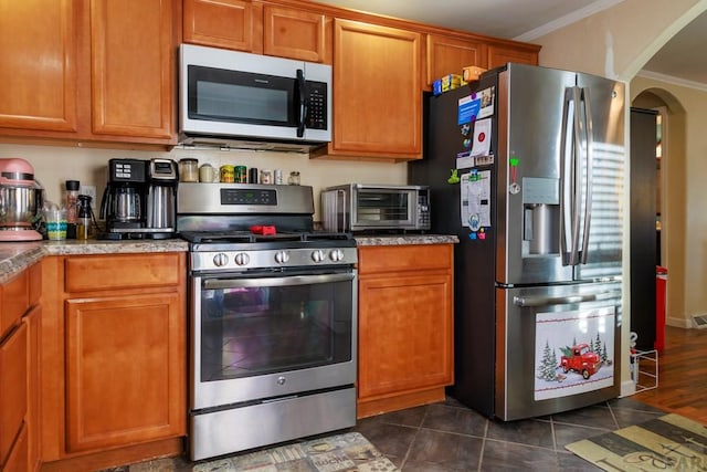 kitchen featuring a toaster, appliances with stainless steel finishes, brown cabinetry, and crown molding