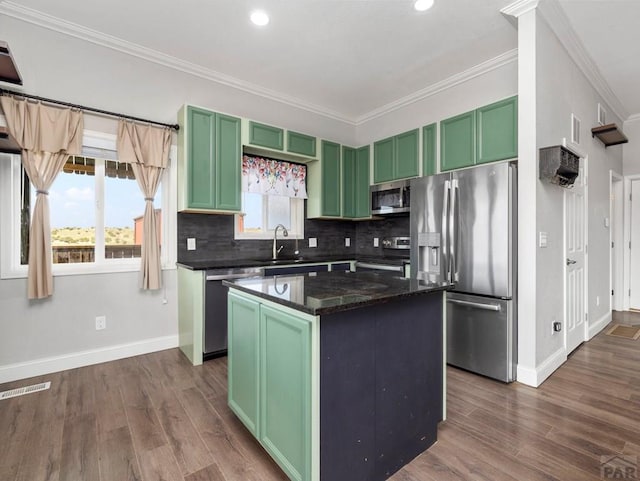 kitchen featuring a kitchen island, appliances with stainless steel finishes, dark stone countertops, green cabinets, and a sink