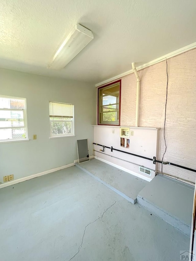 735 Poplar Ave, Las Animas, CO 81054 - empty room featuring unfinished concrete flooring, plenty of natural light, and a textured ceiling